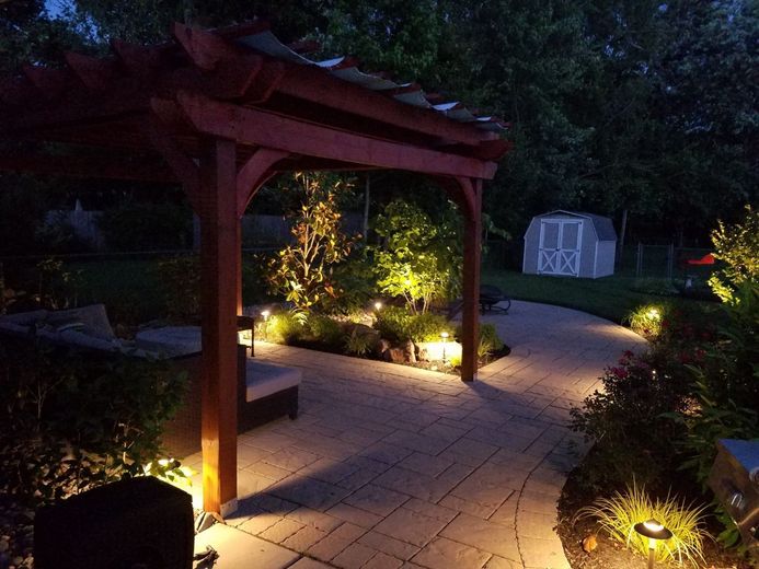 Lit garden path with a wooden pergola, landscape lights, and a small greenhouse at dusk