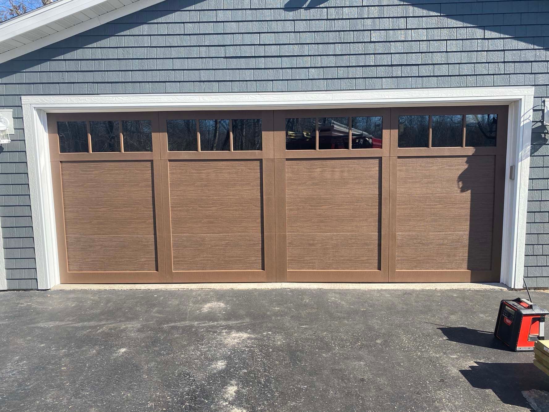 Wooden four-car garage doors in a gray shingled house exterior with a driveway in front