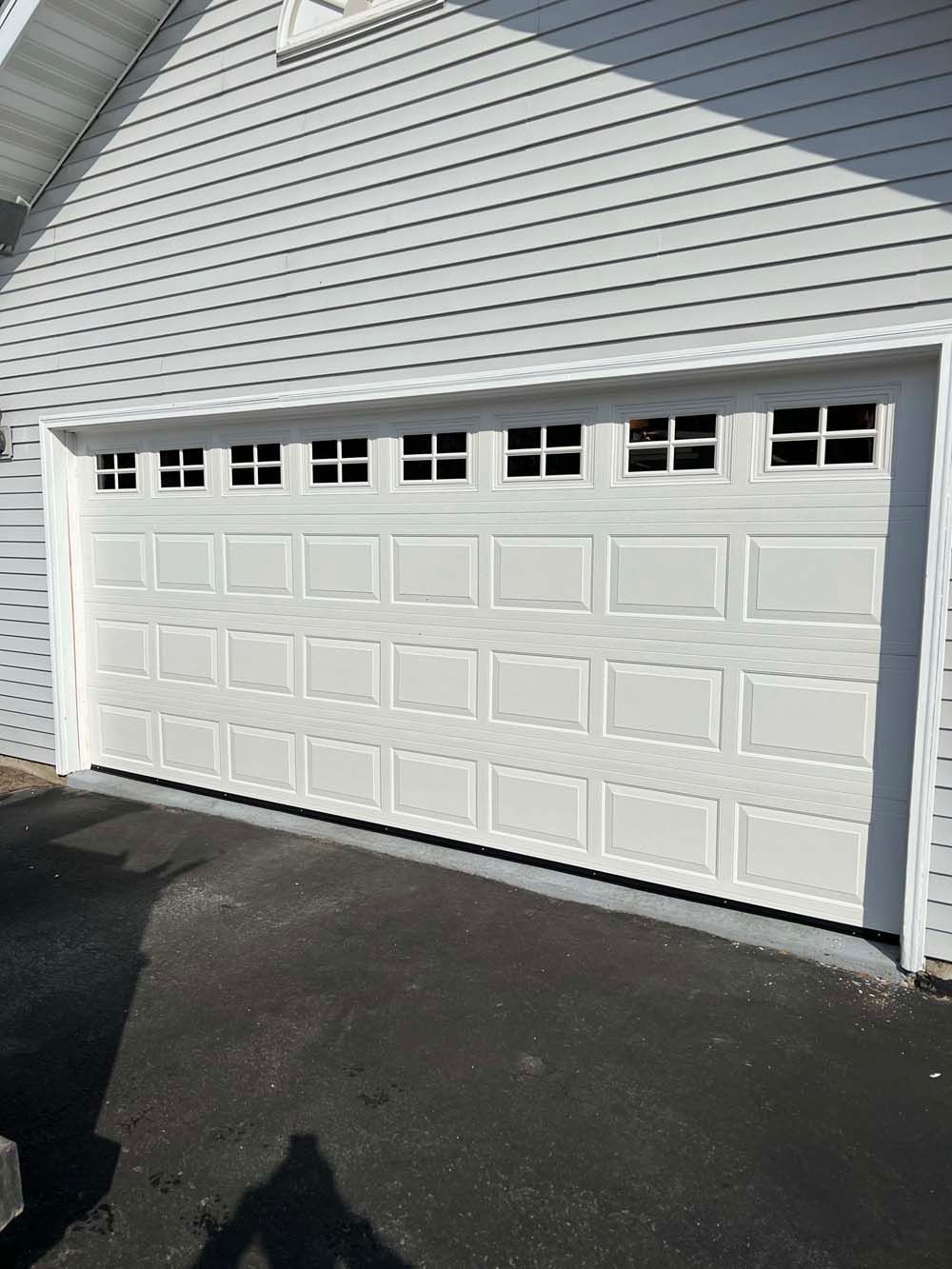 White double garage door with small windows on a house exterior, beside a driveway