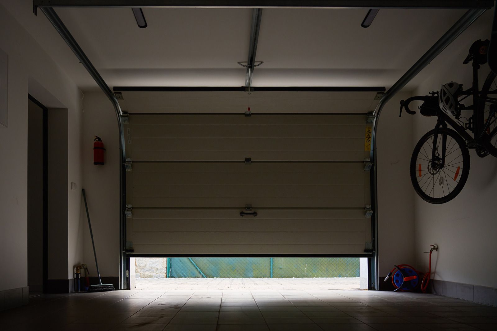 Dim garage interior with a closed white door, bicycles on the right wall, and daylight under the door.