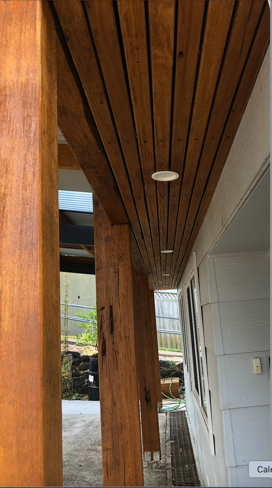 Wooden porch ceiling with a beam and light, viewed down a narrow exterior walkway near a white wall.  — Taddeo Constructions in Kiama Downs, NSW
