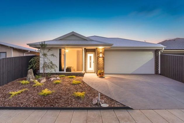 Modern single-story house with a lit entryway, desert landscaping, and a double garage at dusk