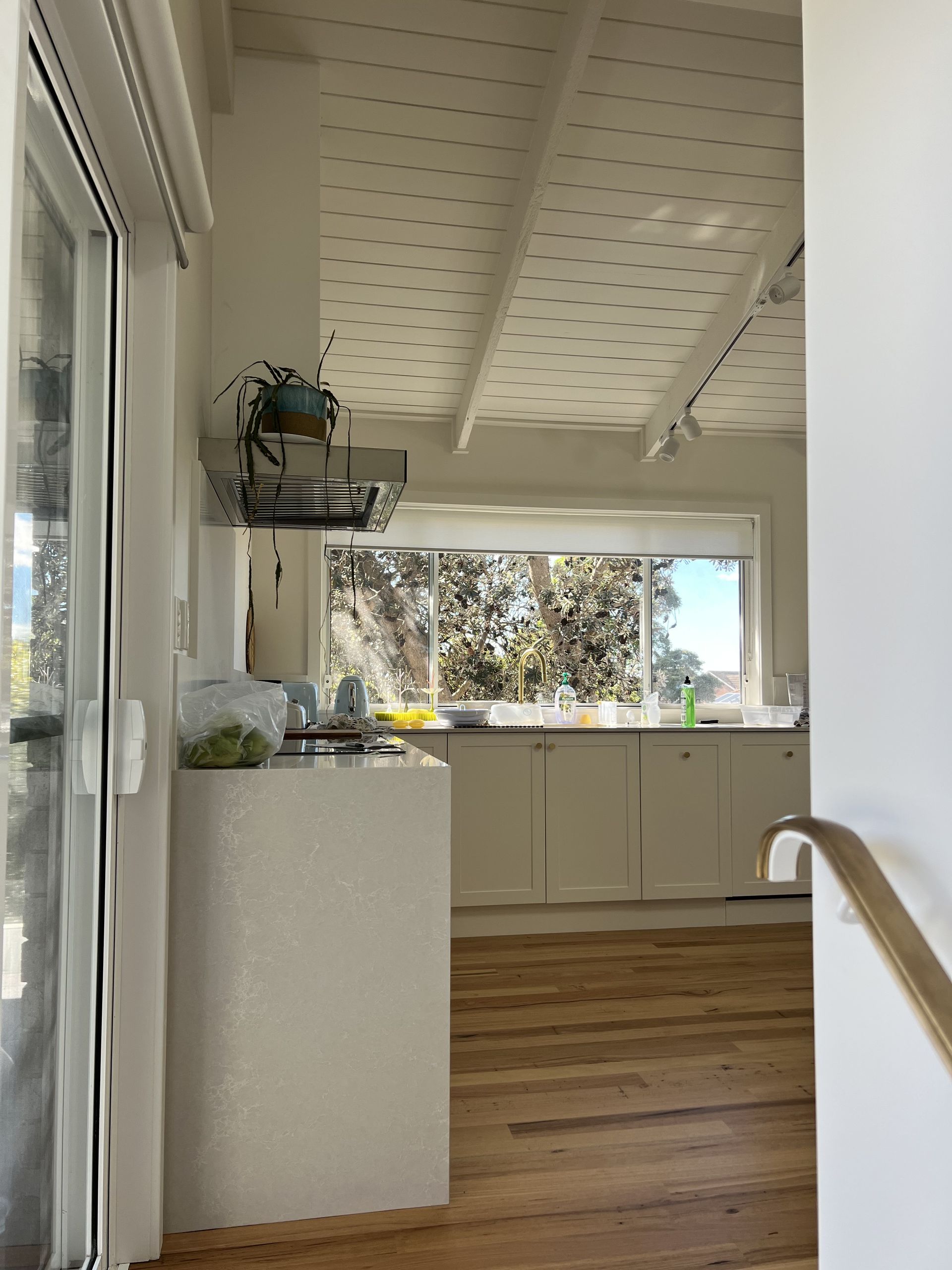 Bright kitchen interior with white cabinets, wood floor, and large window overlooking trees