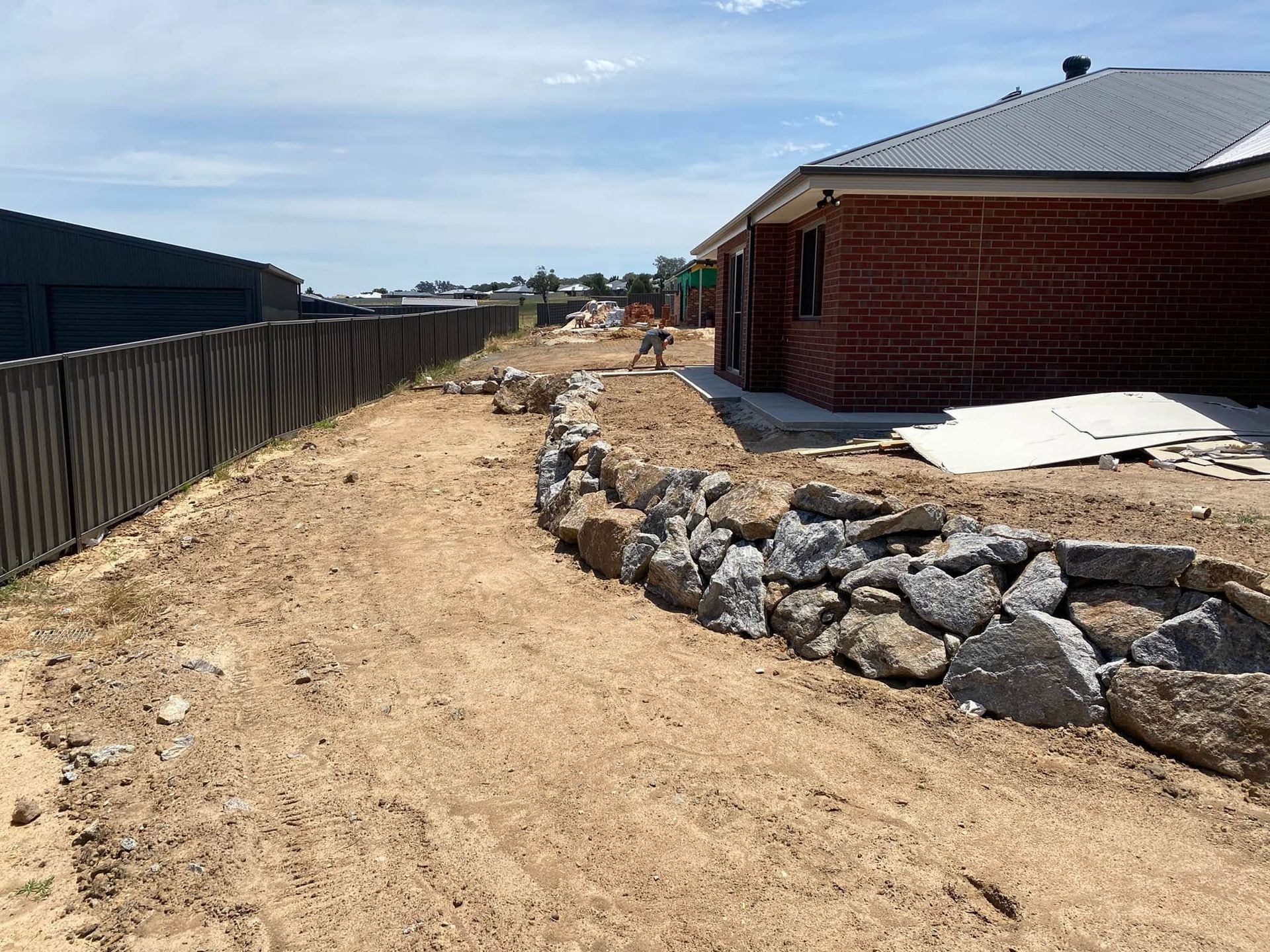 Dirt path beside a red brick house and rock border in a suburban construction area