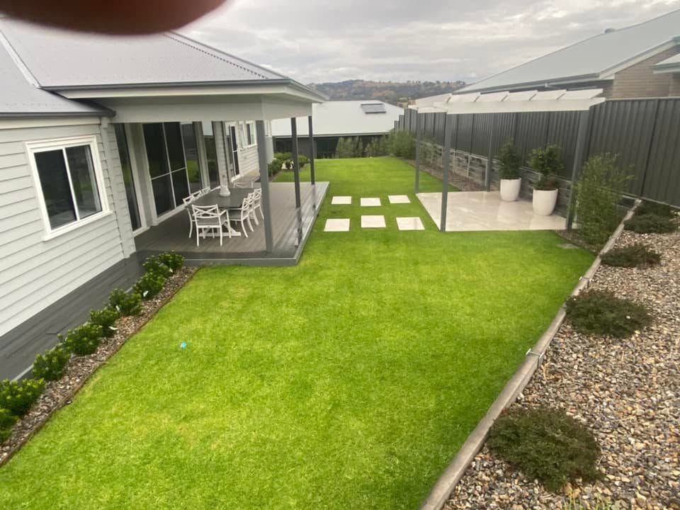 Backyard with green lawn, paved stepping stones, patio chairs, and a gravel border beside a house