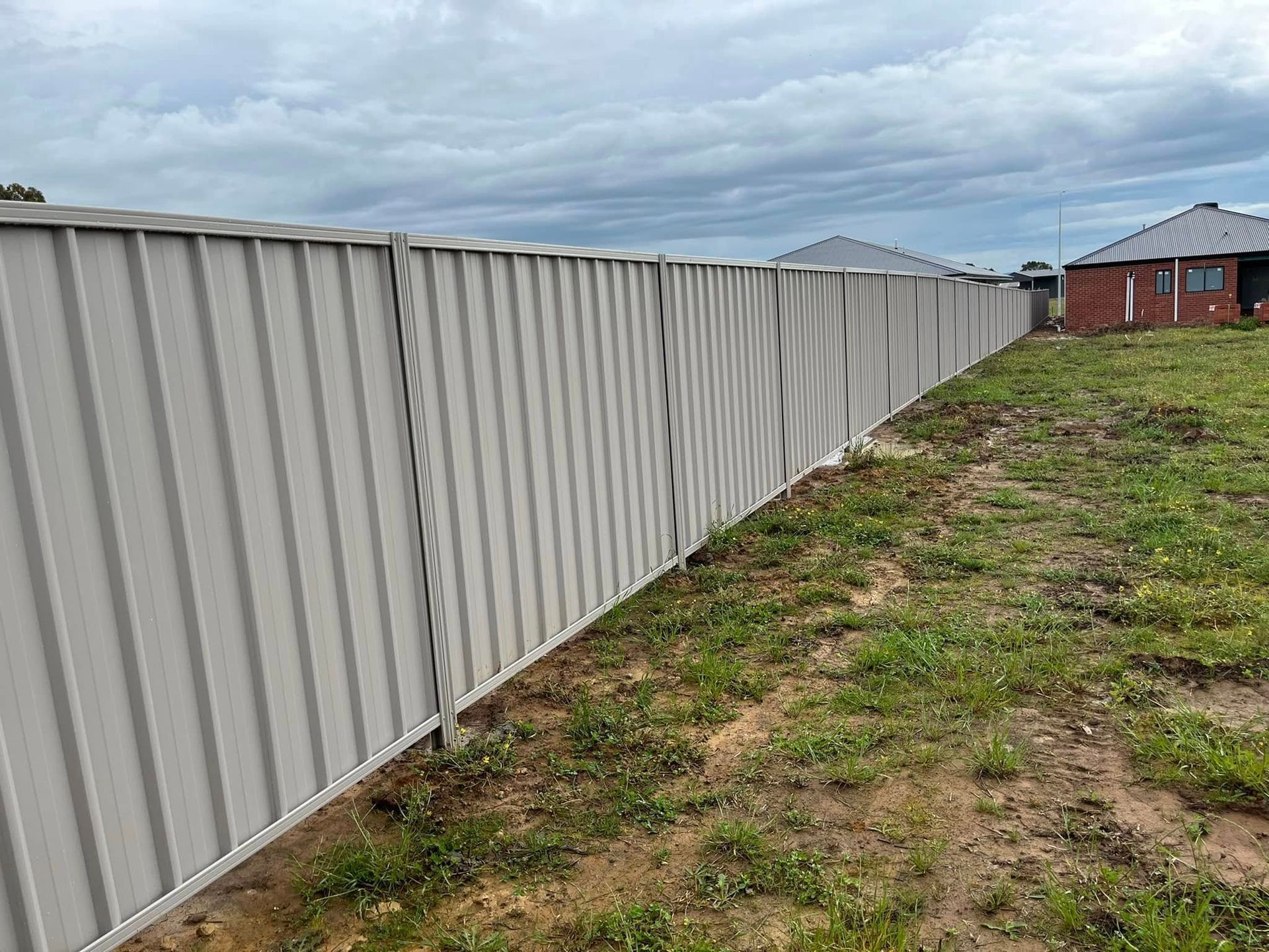 Long gray metal fence along a grassy yard under a cloudy sky