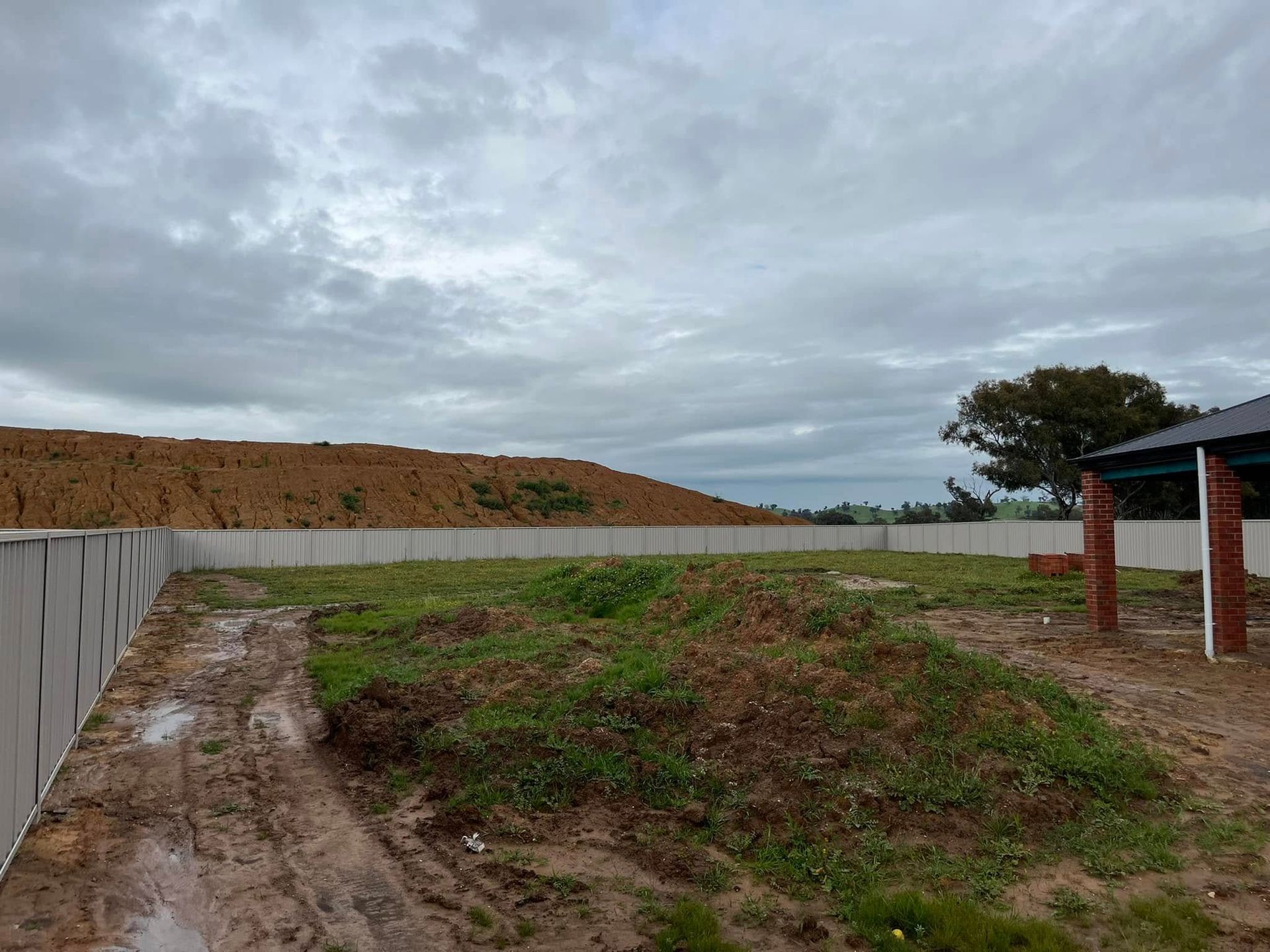 Overcast construction site with dirt mound, bare ground, and a partially built structure on the right
