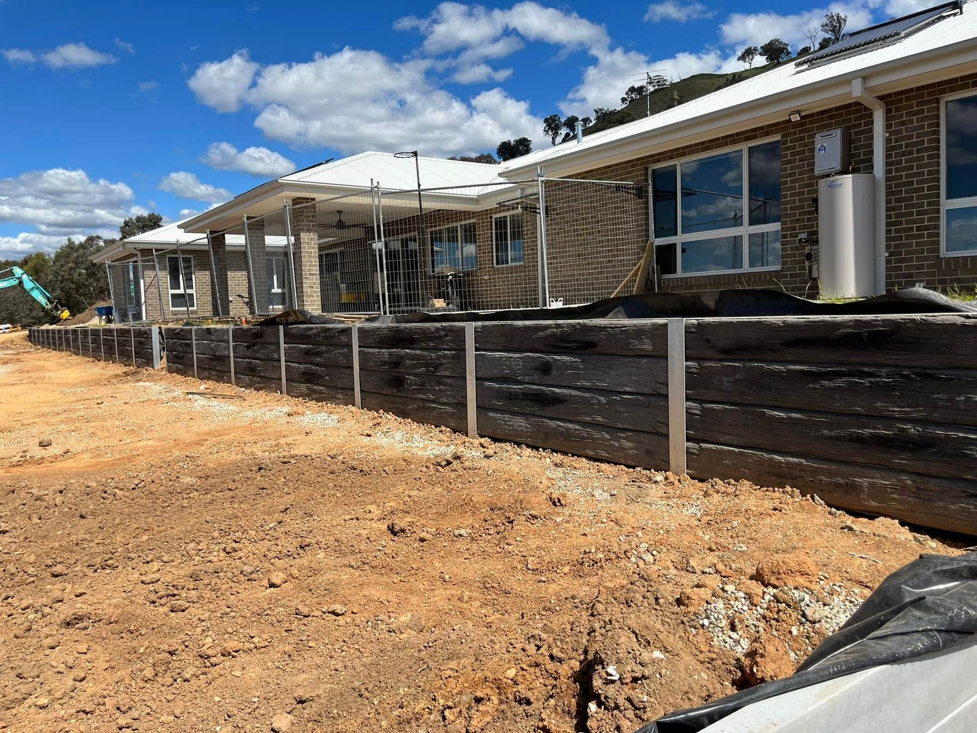 New suburban homes with a dirt lot and temporary fencing under a blue sky