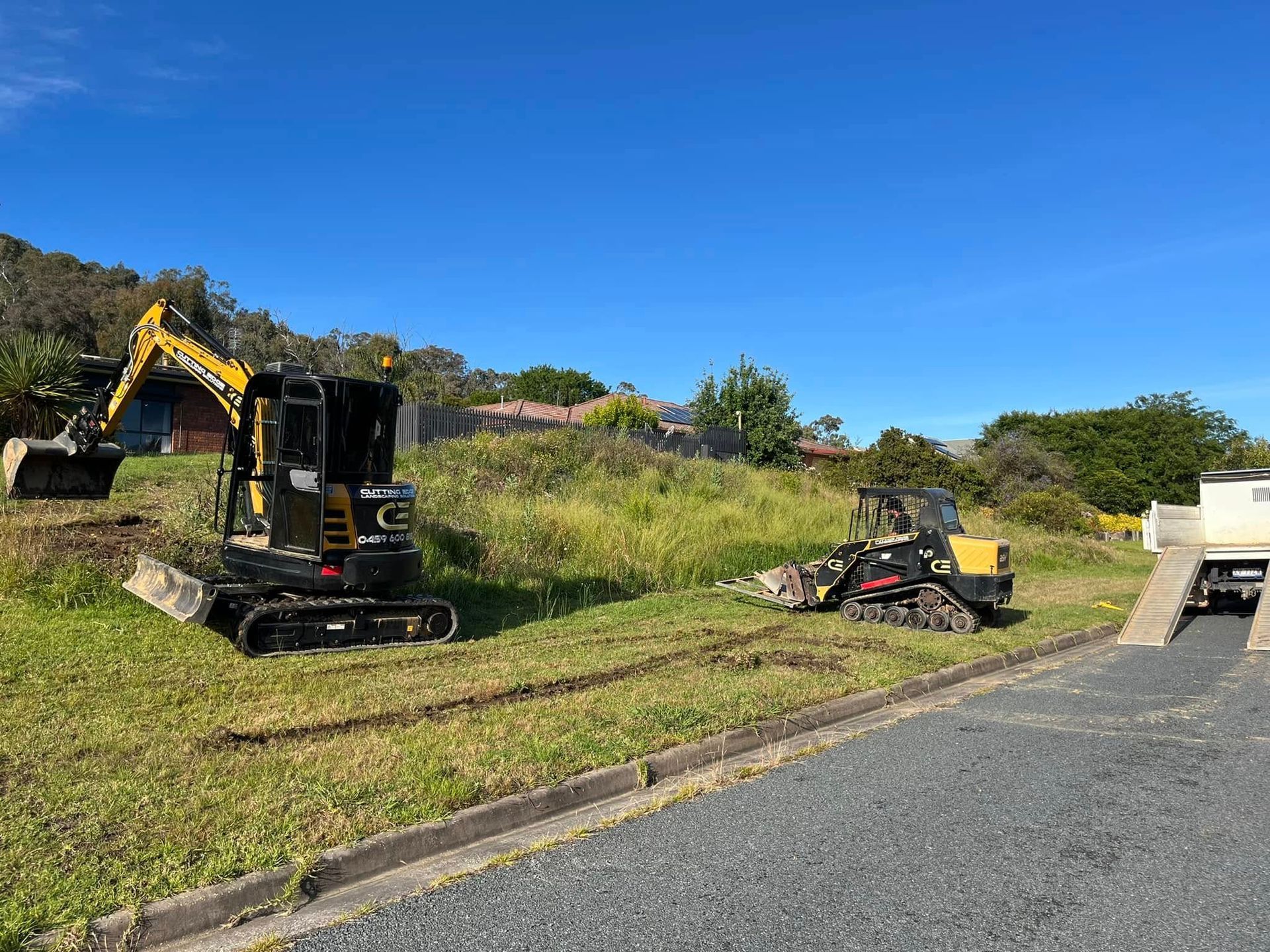 Excavators working on a grassy roadside embankment under a clear blue sky