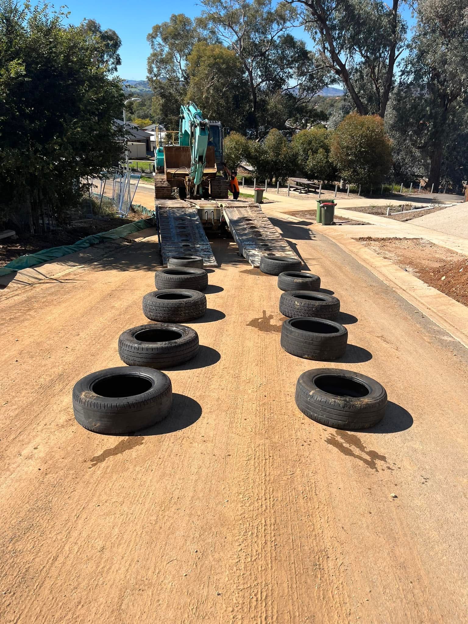 Rows of black tires on a dirt road leading to construction equipment in a wooded area