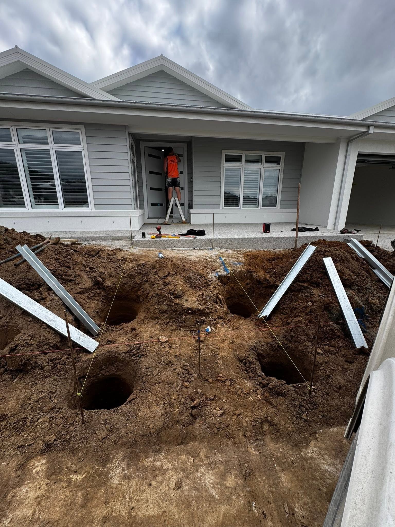 Front yard excavation with dirt piles and pipes in front of a gray house under construction