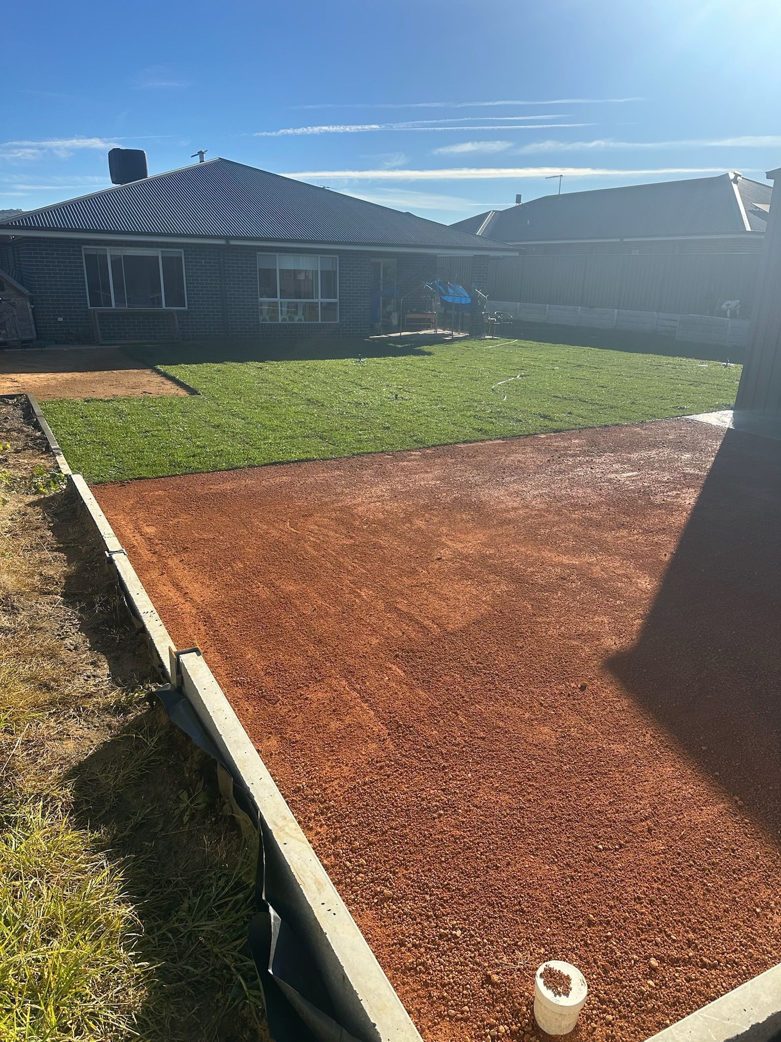 Backyard with red mulch, green grass, and a house under a sunny sky