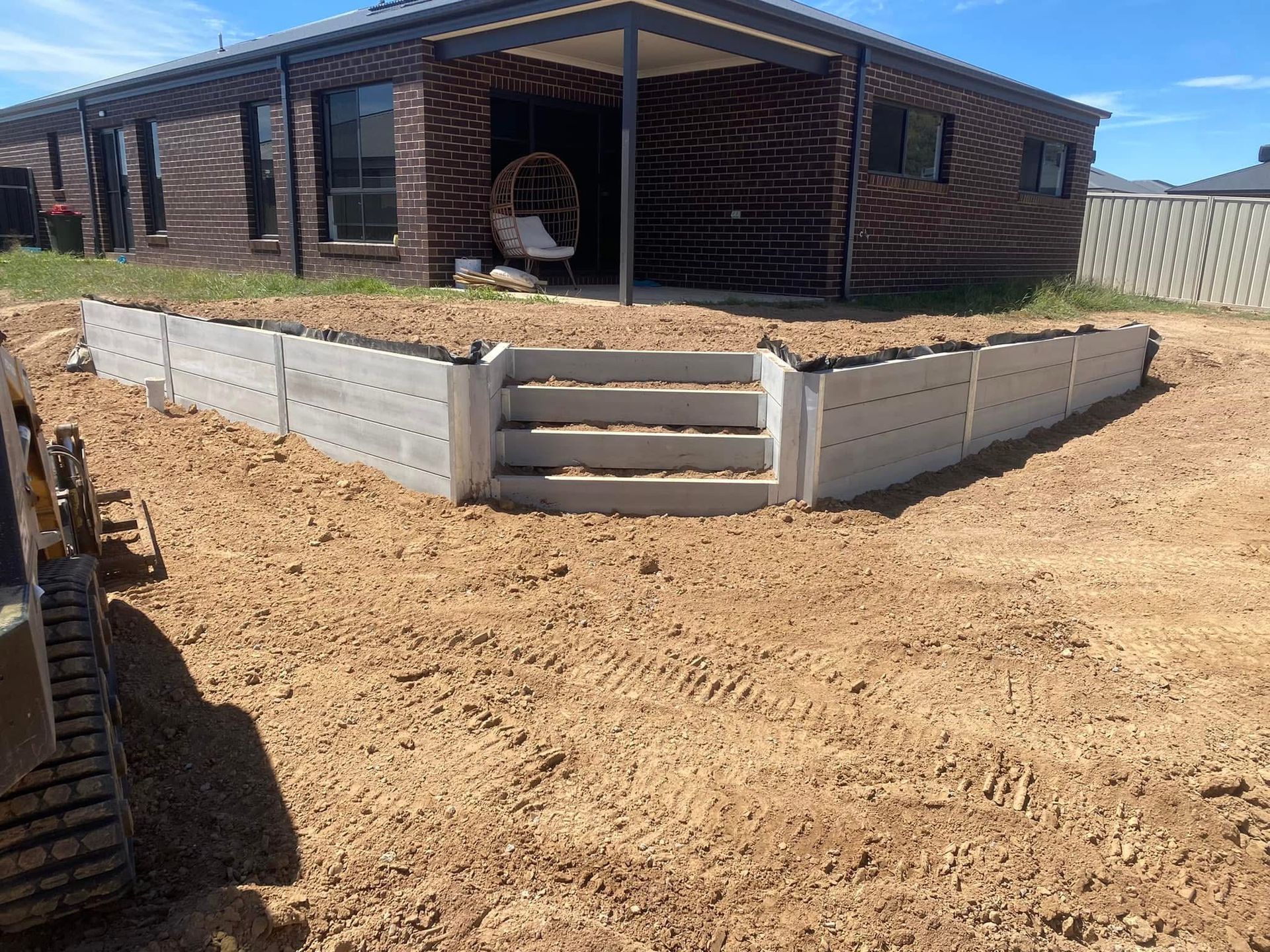 Front view of a brick house with a low gray retaining wall and dirt yard under construction