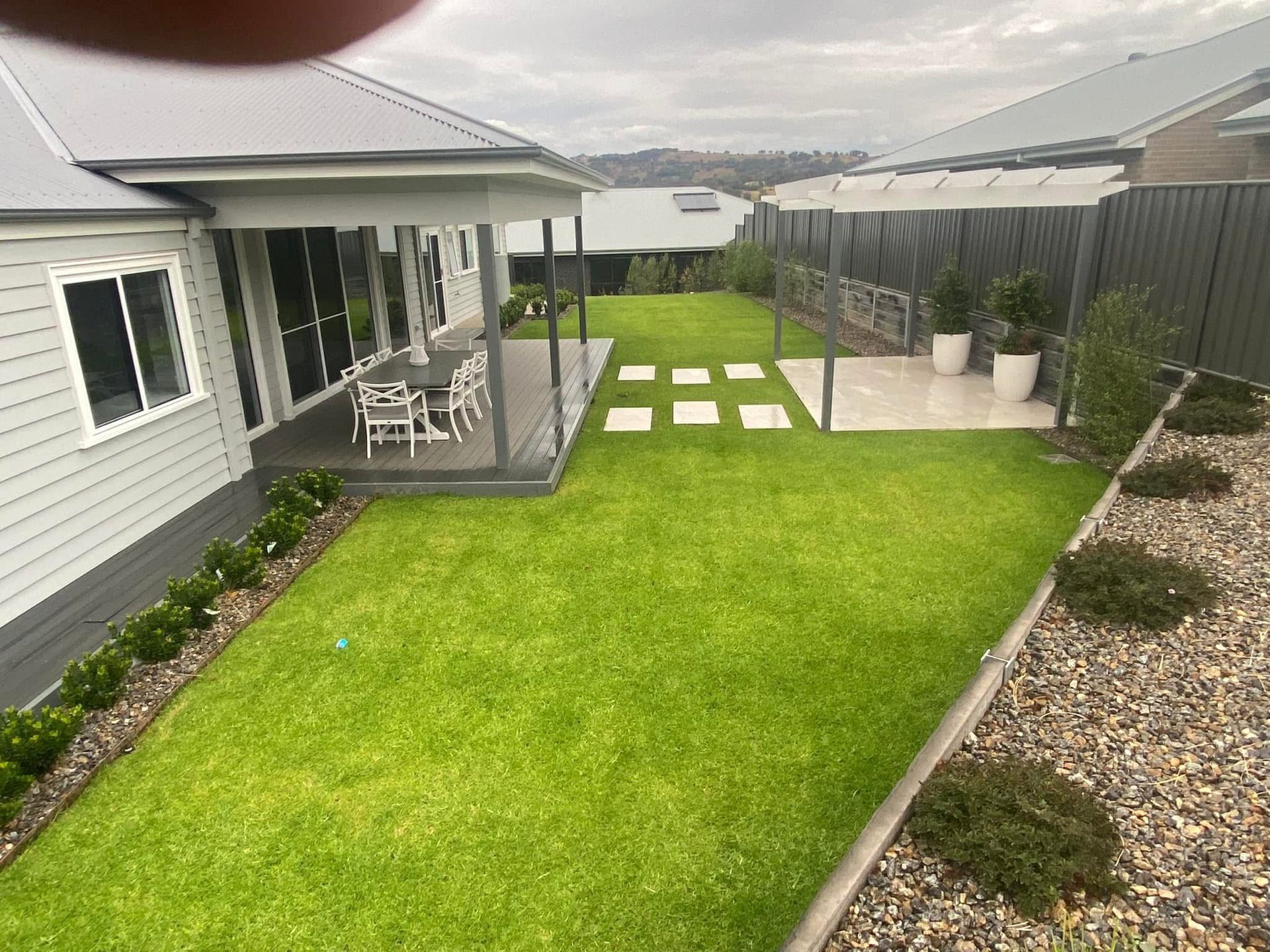 Backyard with green lawn, stone stepping path, patio seating, and gravel border beside a house