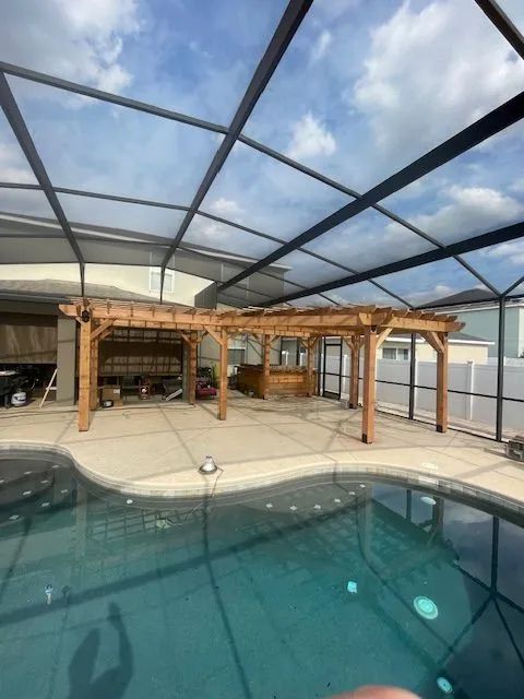 Pool area with brown pergola structures under a screened enclosure; blue pool in foreground.