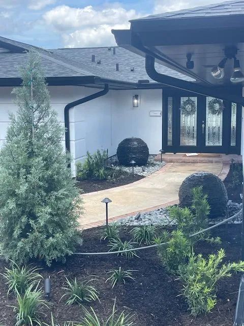 Backyard with artificial green grass, stone retaining wall, and house in the background.