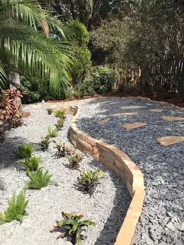 Stone path and planting beds in a garden, edged with a curved retaining wall.