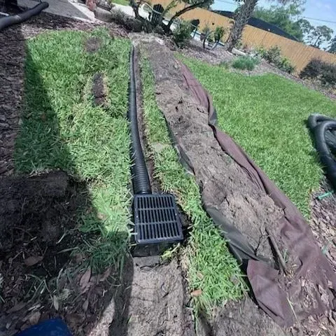 Installation of a black drainage system in a grassy yard.