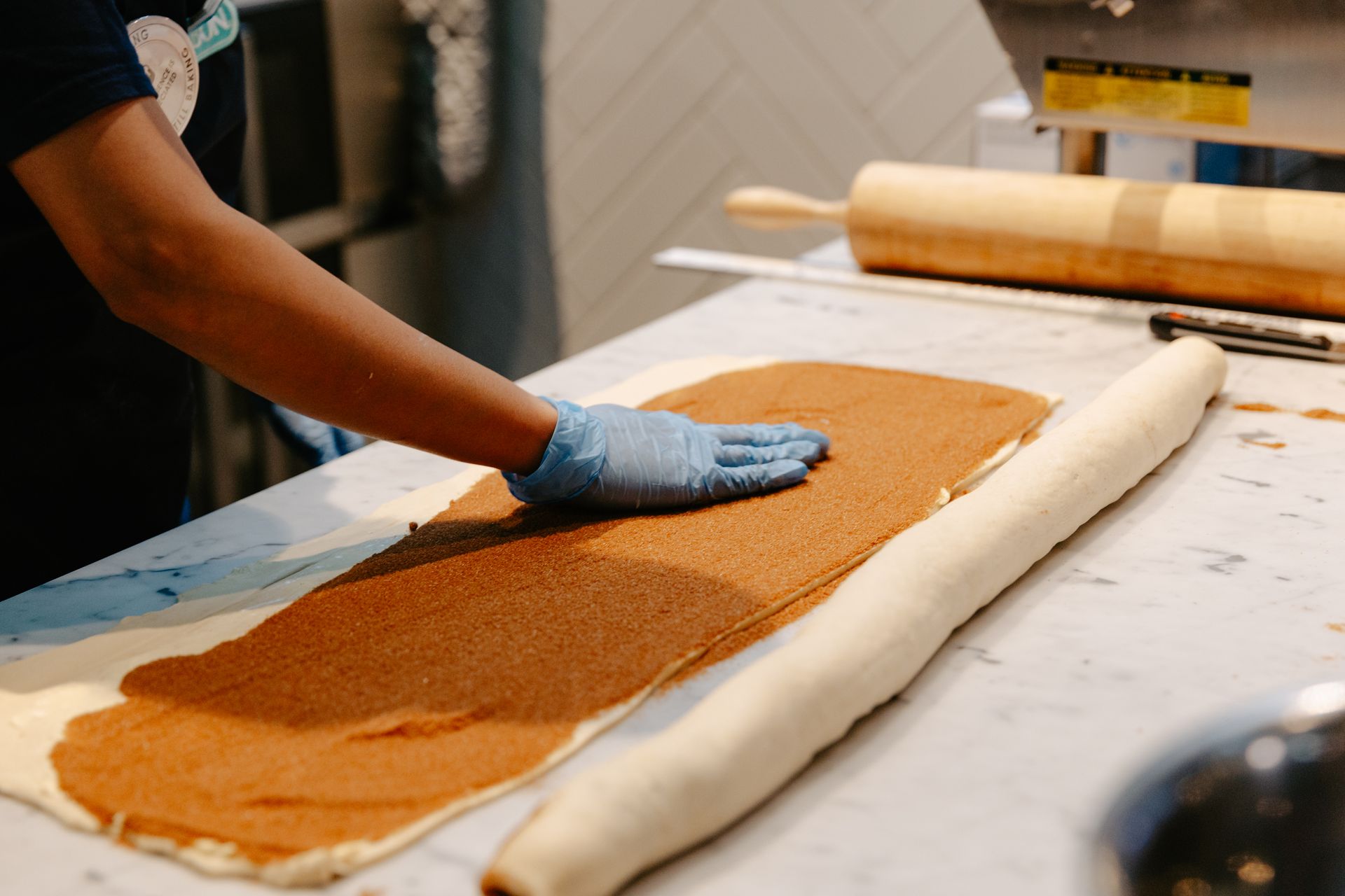 Worker spreading brown filling on rolled dough at a bakery prep table