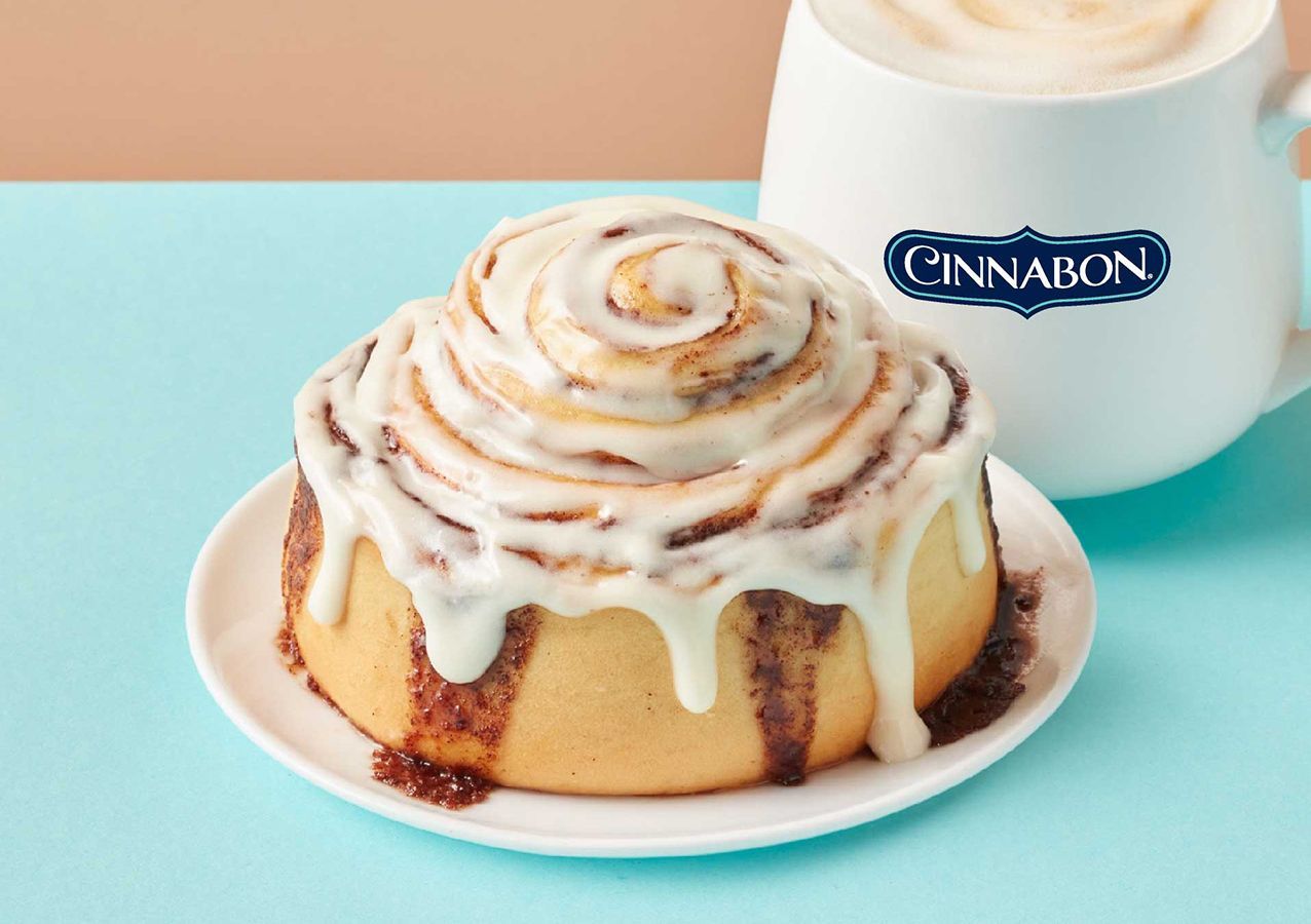 A cinnamon roll on a plate next to a cup of coffee