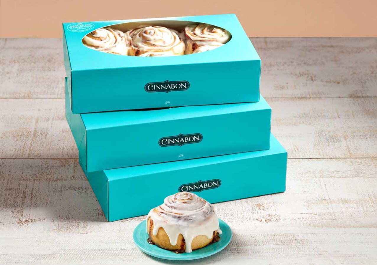 Three boxes of cinnamon rolls are stacked on top of each other on a table.