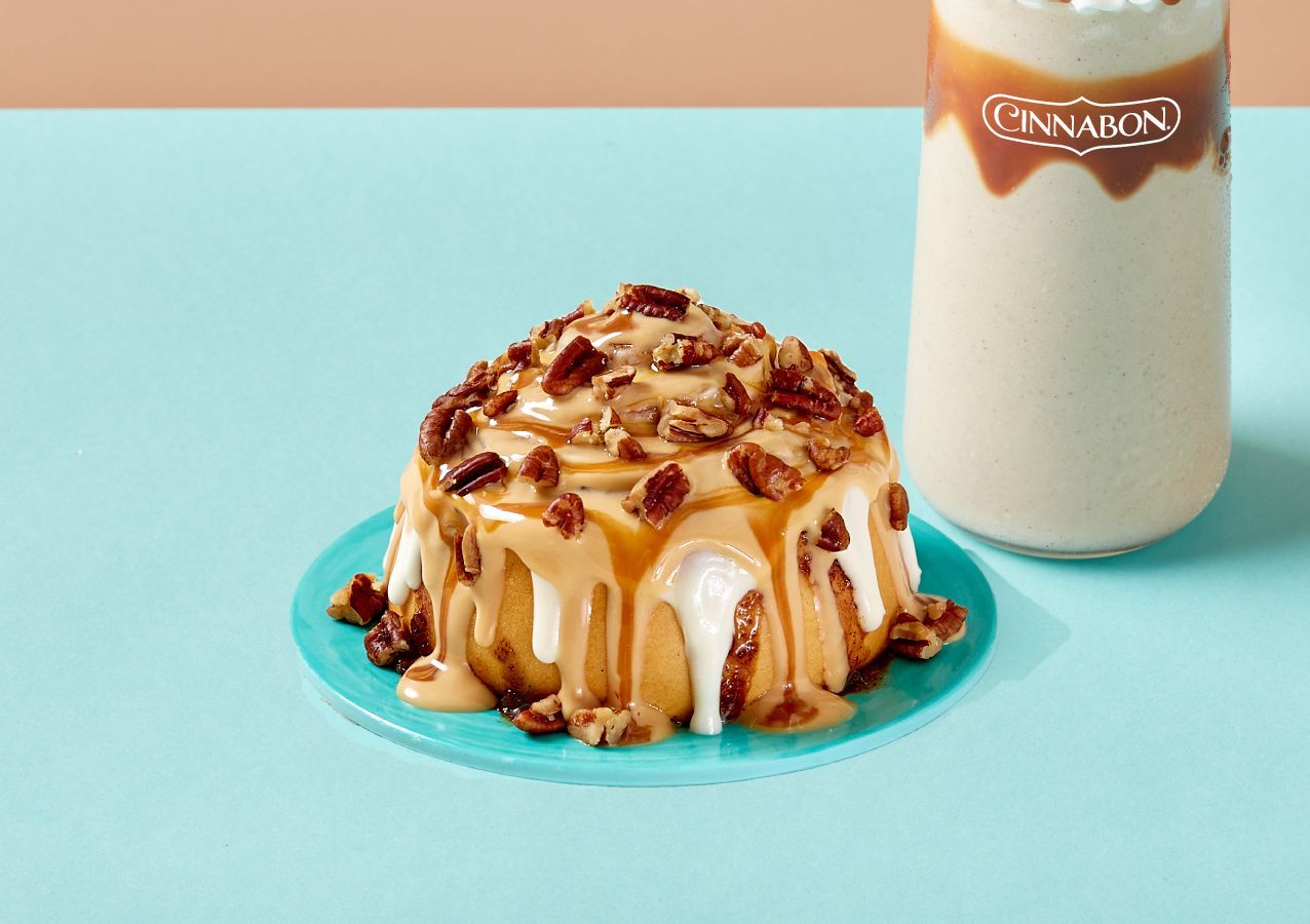A cinnamon roll is sitting on a blue plate next to a glass of milk.
