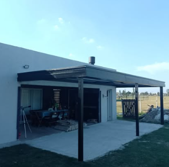 Peque&ntilde;o patio moderno con techo blanco y postes negros, junto a un jard&iacute;n con c&eacute;sped bajo un cielo azul despejado