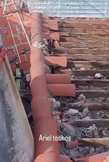 Tejas rojas da&ntilde;adas, con escombros y vigas de madera a la vista en un tejado