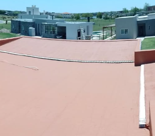 Terraza en la azotea con suelo rojo, un muro bajo y edificios grises modernos con vistas a un paisaje verde.
