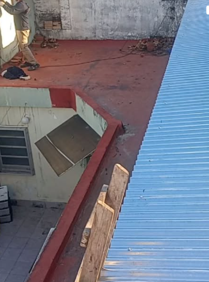 Azotea con hormig&oacute;n rojo, un techo de chapa ondulada azul y una tabla de madera apoyada contra una pared.