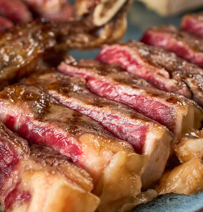 Close-up de fatias de bife grelhado com o centro rosado e a crosta dourada.