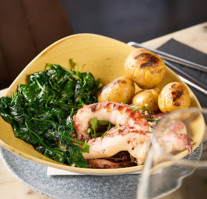 Tigela de salada de frutos do mar com verduras, batatas e polvo grelhado sobre uma mesa