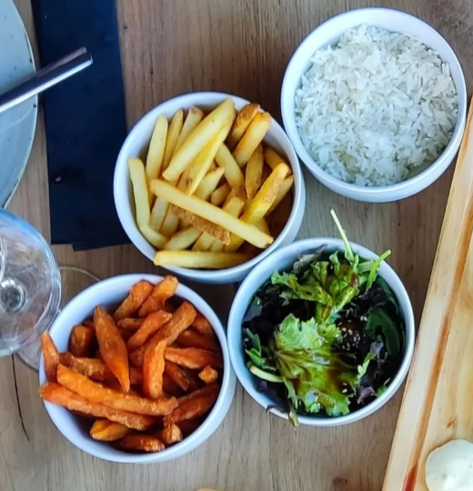 Três tigelas de batatas fritas, arroz branco e salada mista sobre uma mesa de madeira.