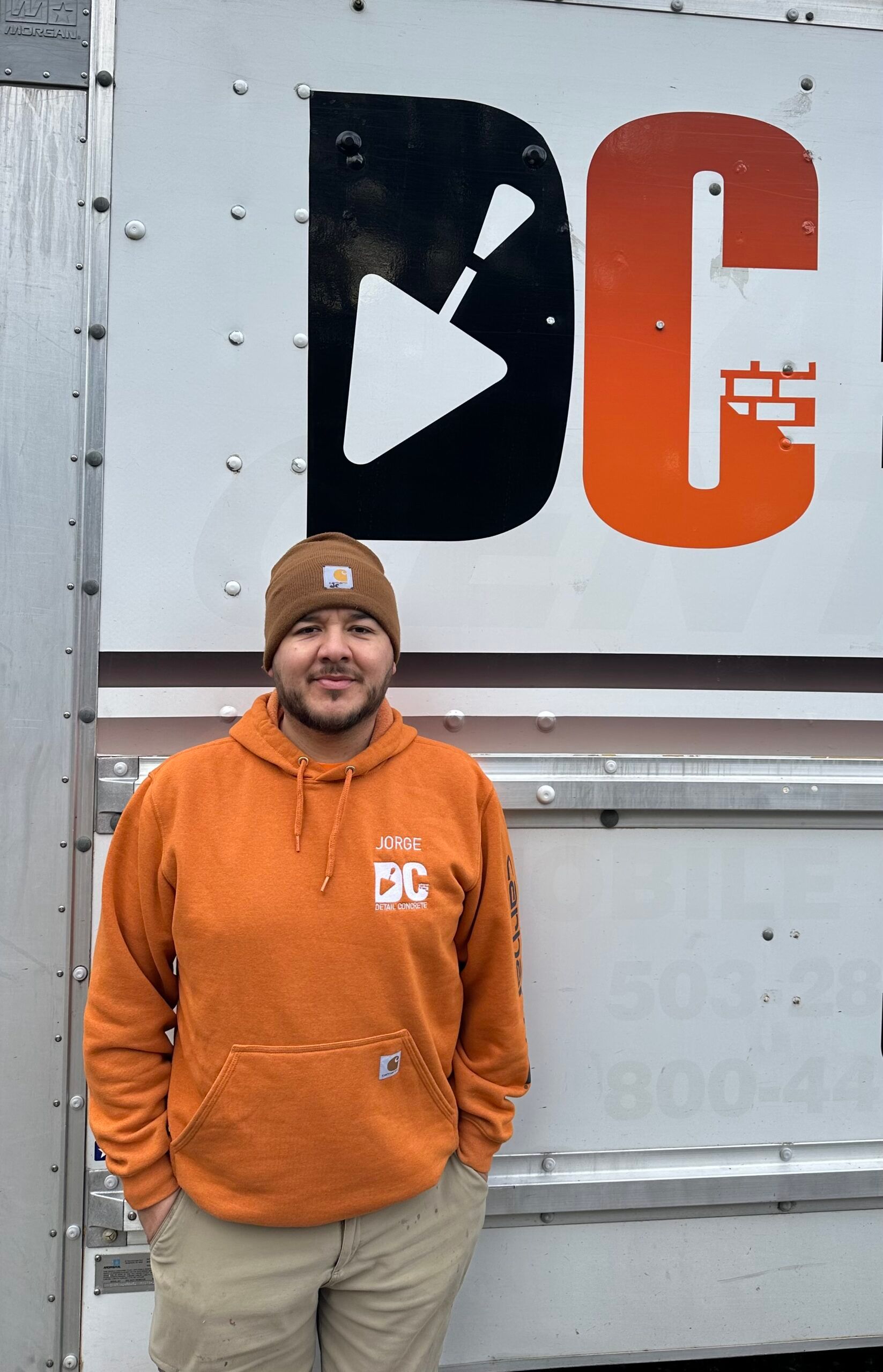a man in an orange hoodie is standing in front of a white truck of Detail Concrete.