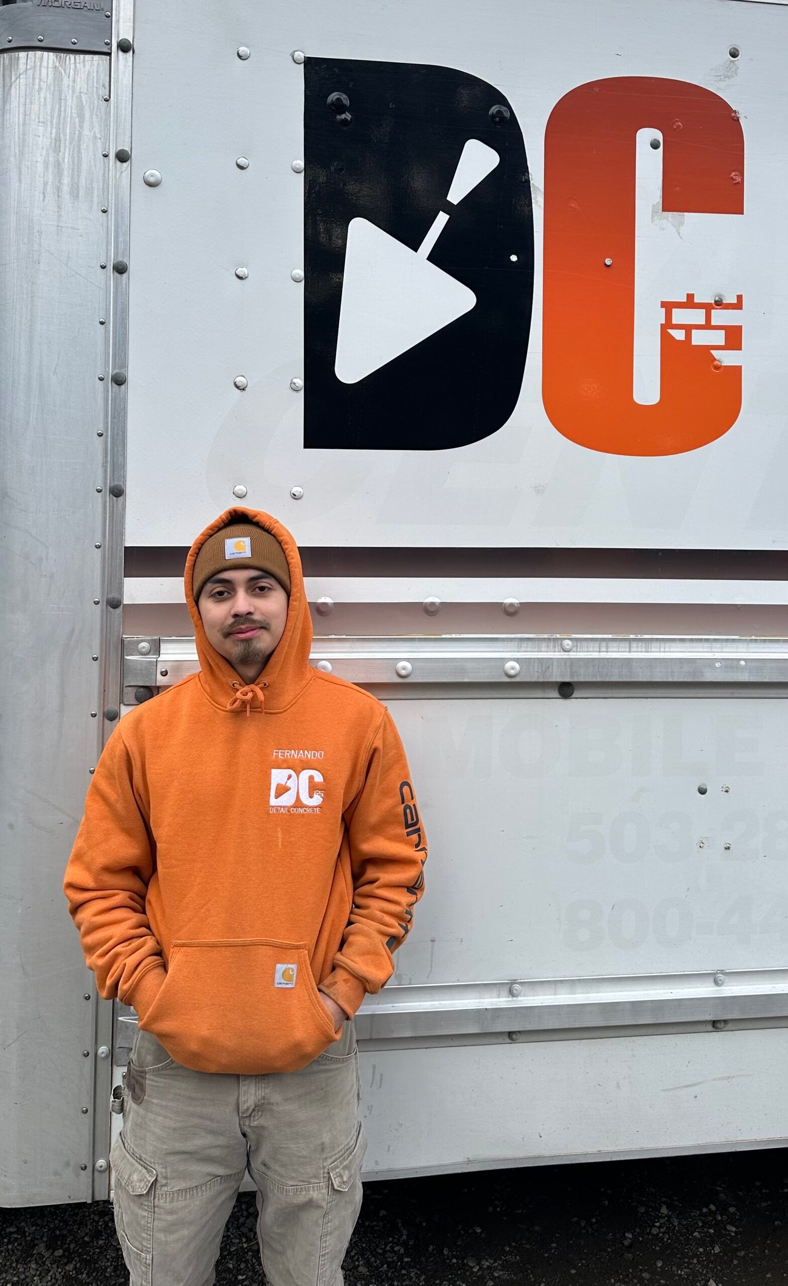 a man in an orange hoodie is standing in front of a truck .