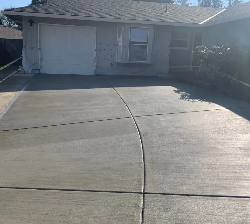 Newly poured concrete driveway in front of a light gray house with a garage and window.