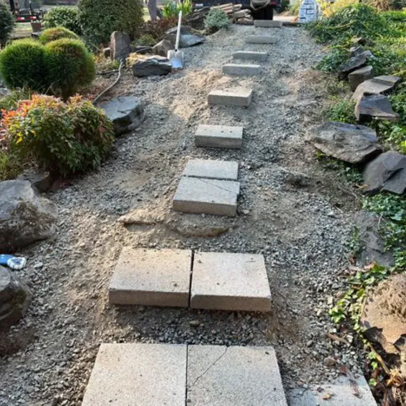 Stone stepping stones on a gravel path through a garden, with bushes and rocks alongside.
