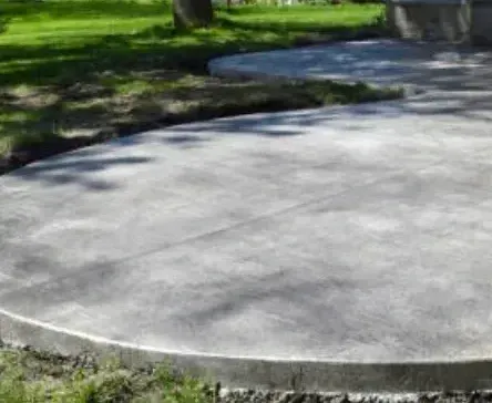 Concrete driveway beside a white house and green lawn under trees.