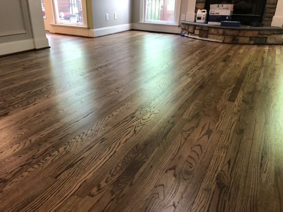 Glossy, stained hardwood floor with natural wood grain. Fireplace visible in the background.