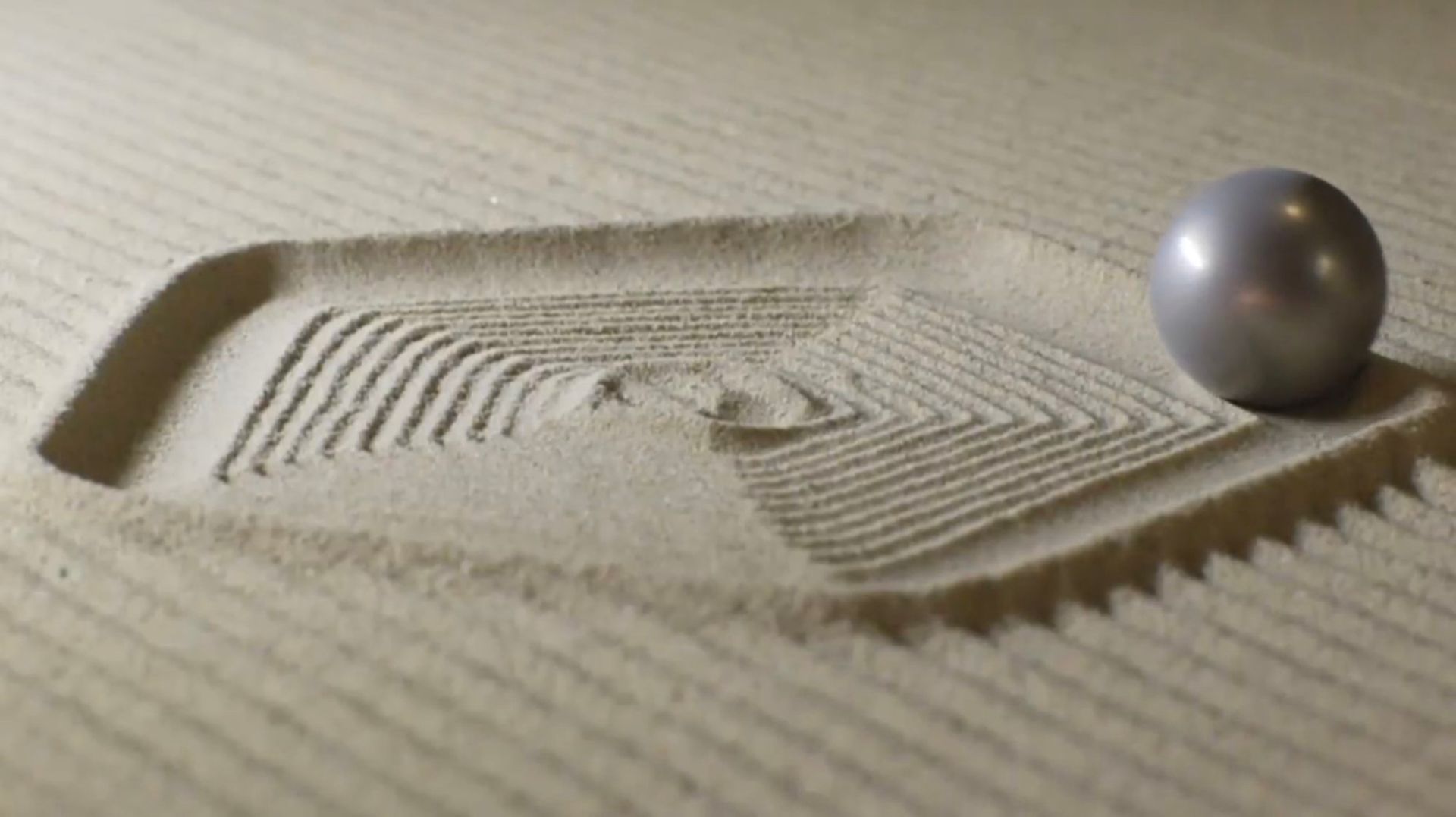Metallic ball on a sand tray with patterns raked into the sand.