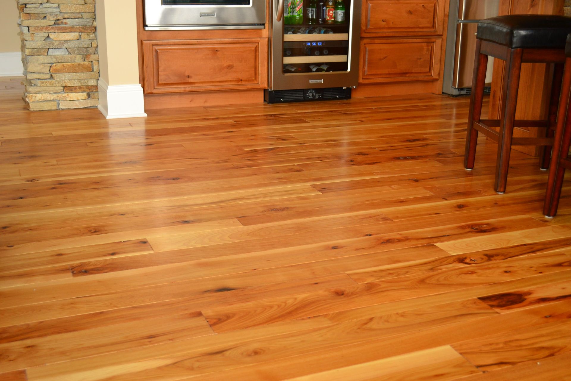 Hardwood floor in a kitchen with wooden cabinets, a wine cooler, and a bar stool.