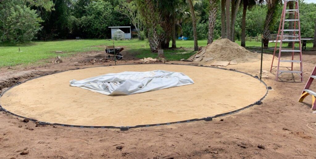 A circular sand base for a pool construction site, with a white tarp covering the center.