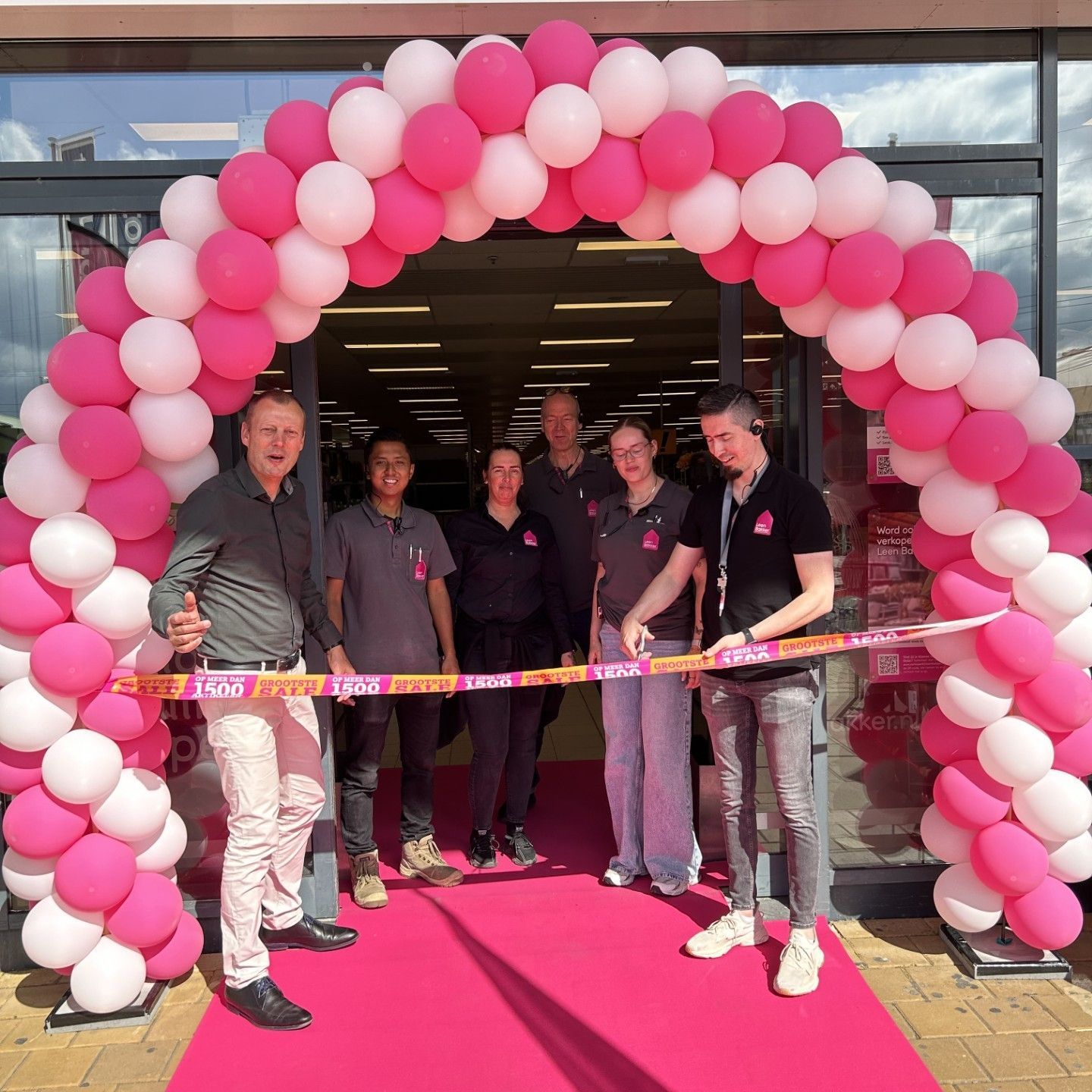 Mensen staan ​​onder een roze-witte ballonnenboog bij de opening van een winkelpand.