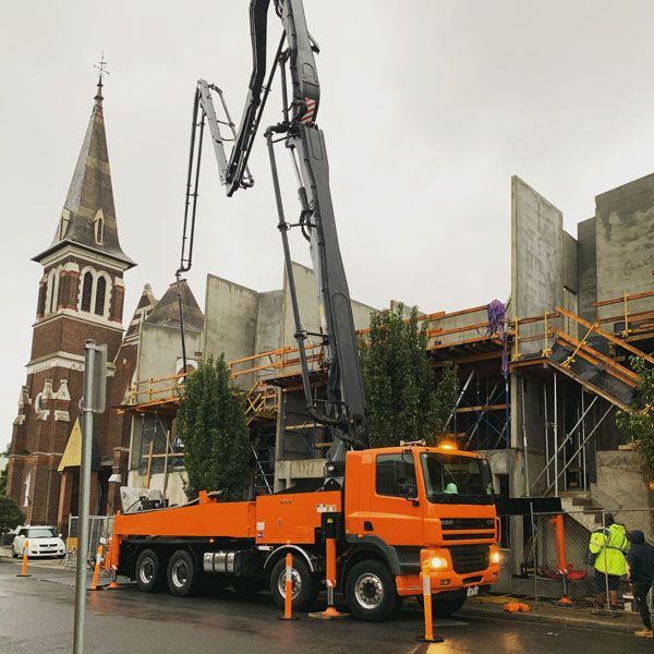 An orange truck is parked in front of a building under construction