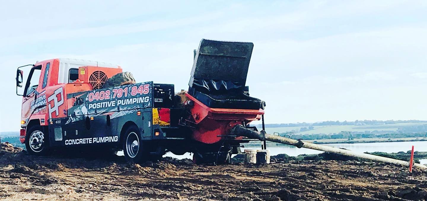 A truck with a pump attached to it is parked in a dirt field.