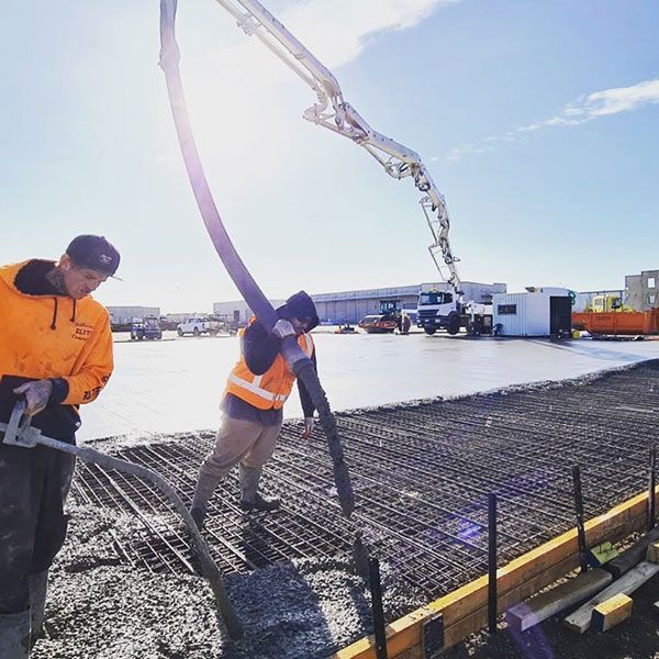 Two men are working on a construction site with a concrete pump