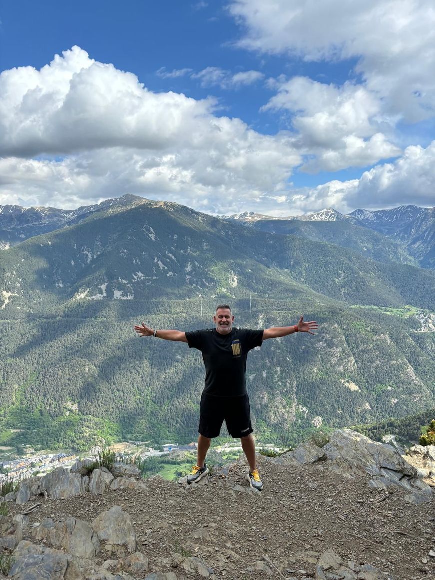 Un hombre está parado en la cima de una montaña con los brazos extendidos.