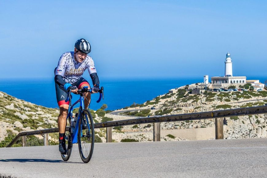 Un hombre va en bicicleta bajando una colina con un faro al fondo.