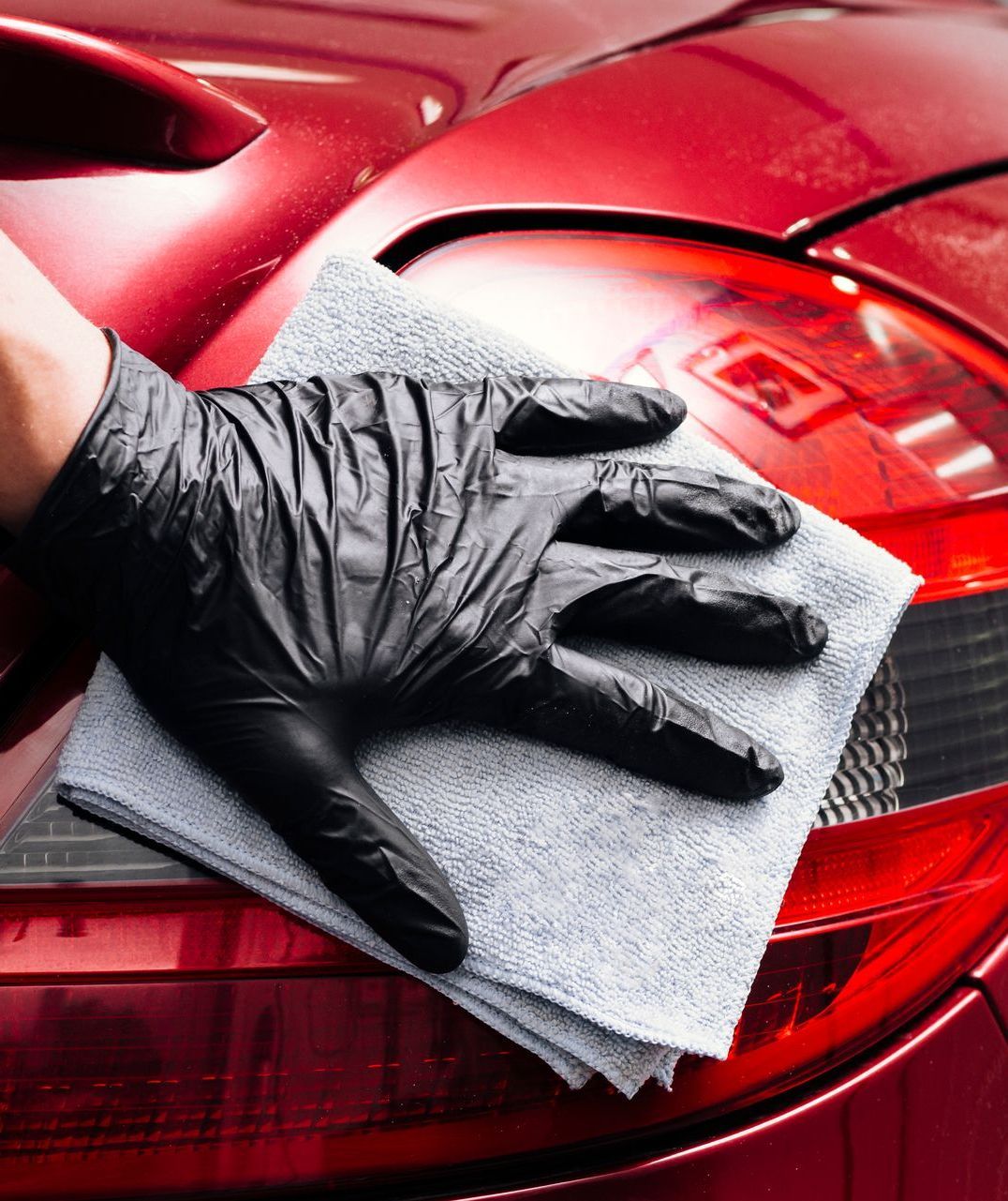 A person wearing black gloves is cleaning a red car with a cloth.