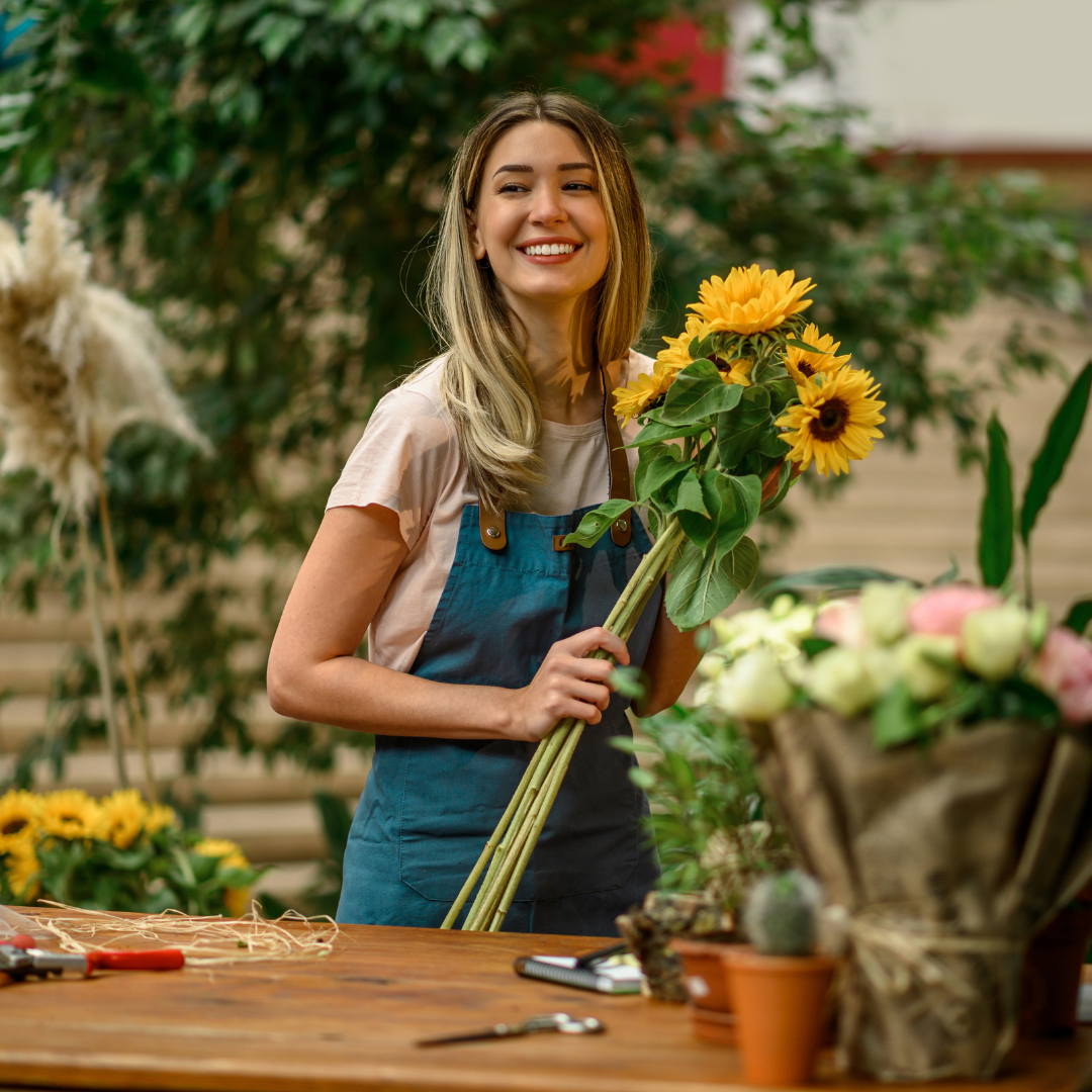 A woman is standing at a table holding a bouquet of flowers.